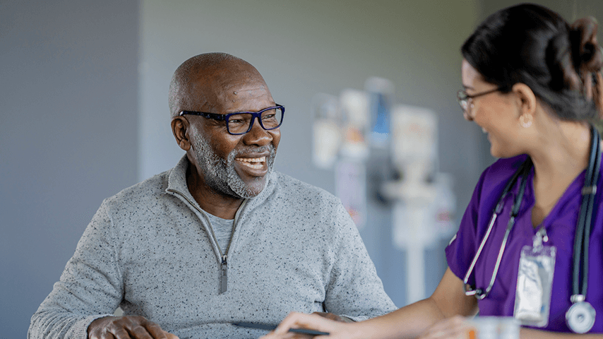 smiling older black man wearing glasses and smiling woman in purple medical scrubs with stethoscope