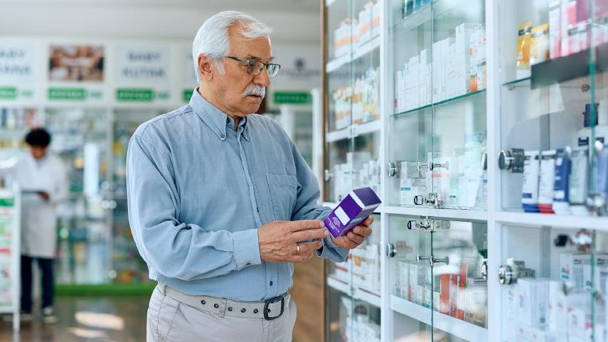 A senior man in a denim shirt is in a store looking to buy an OTC hearing aid.