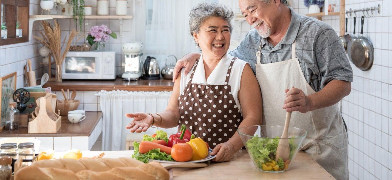 A older Asian couple embracing while preparing a healthy meal in their kitchen