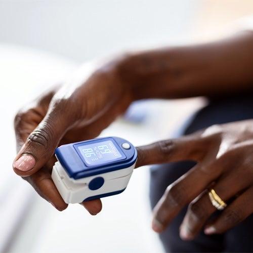 A person’s hands with one finger inserted into a pulse oximeter
