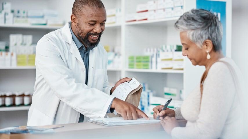 A pharmacist is helping an older Hispanic woman fill out a form before giving her the prescriptions she filled.