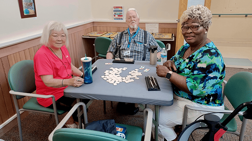two older women and one older man playing mahjong at a gray table