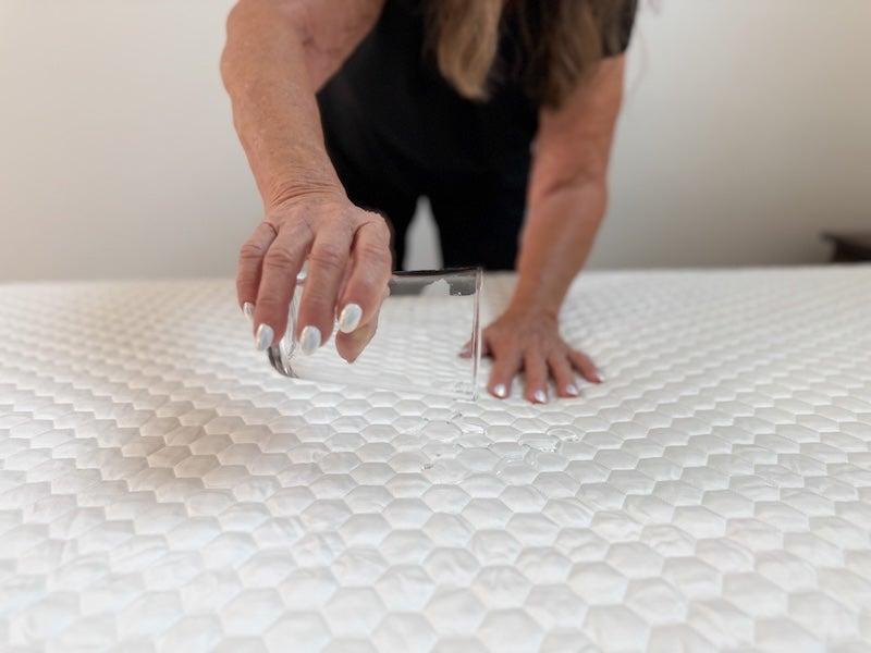 A woman pours water on the Nolah GlacioTex Waterproof Mattress Protector
