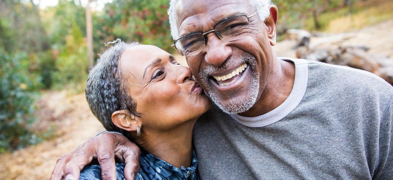 A Black senior couple is outside taking a selfie together in the park.
