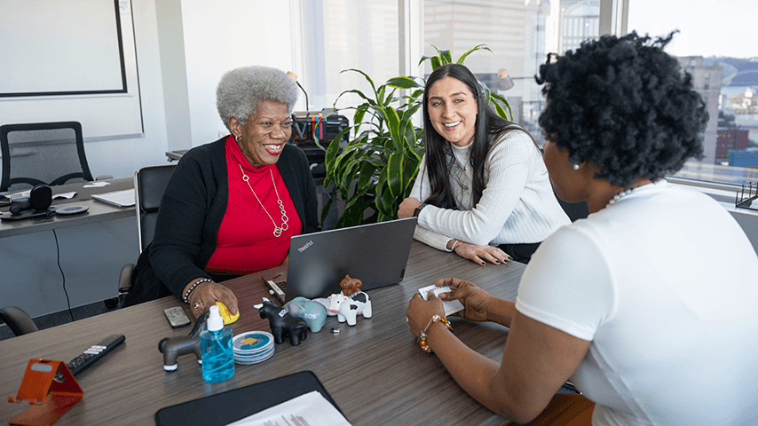 three smiling women at conference table