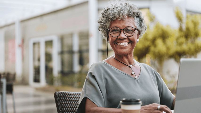 smiling older black woman wearing glasses and sitting outside with laptop