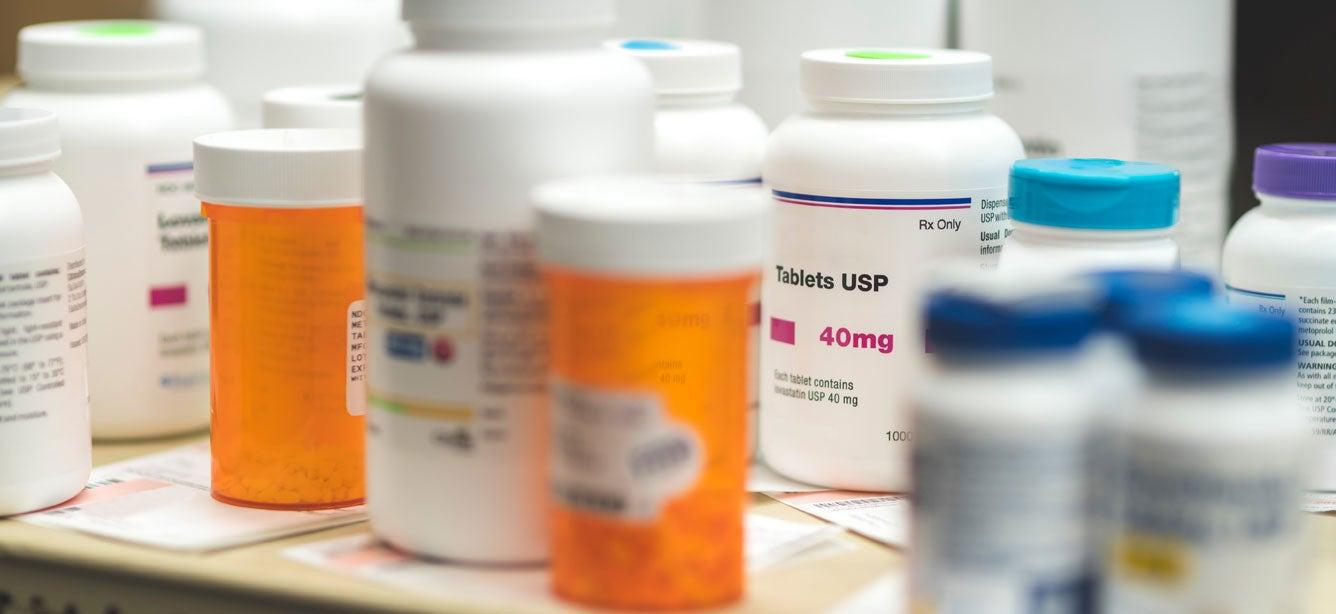 Several prescriptions and pill bottles are on a countertop in a pharmacy storage area.