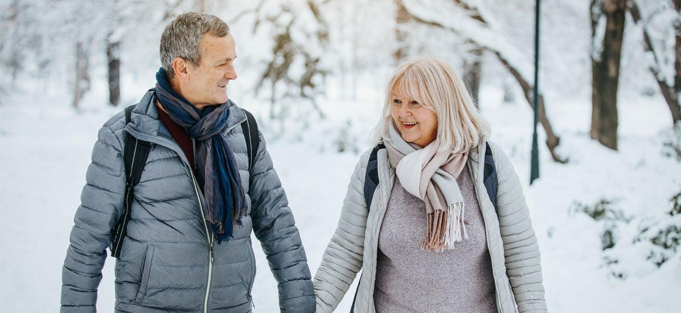 Older man and woman smiling at each other as they walk in the snow
