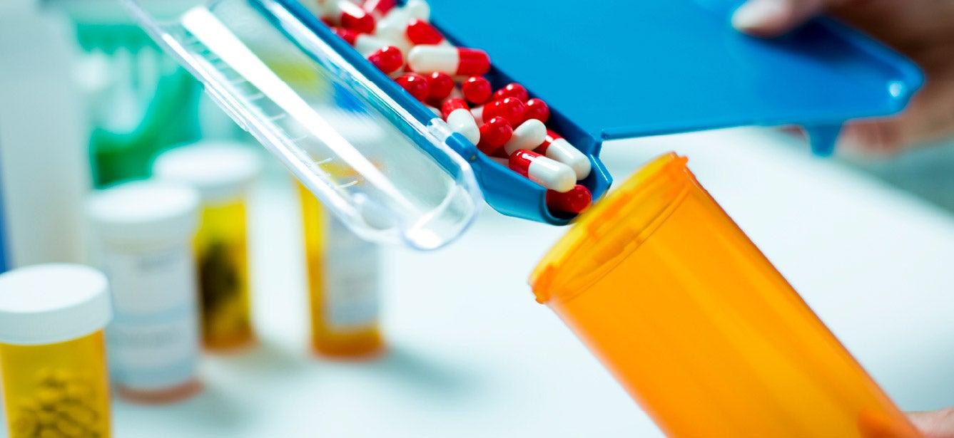red and white pills being poured from into a pill bottle, other pill bottles in the background