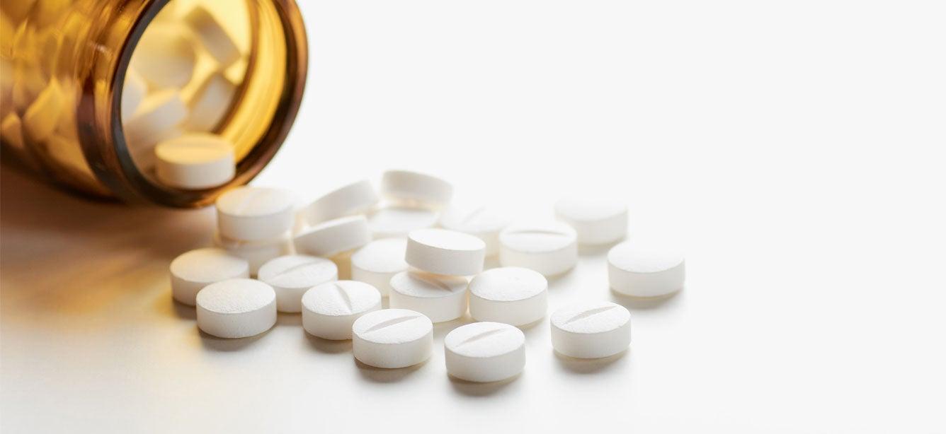 A brown pill bottle tipped over with several round white pills scattered around it on a light surface.