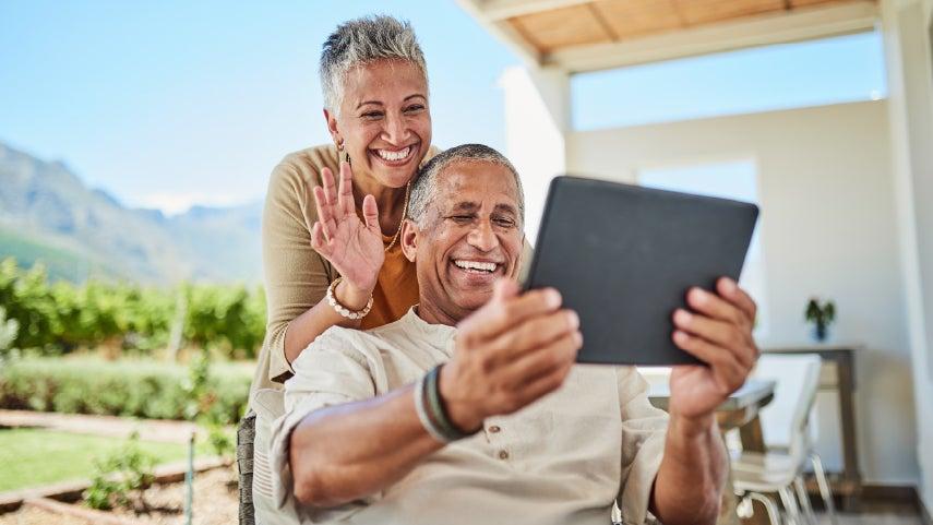 A happy Hispanic couple is sitting outside having a video conference call with a family member.