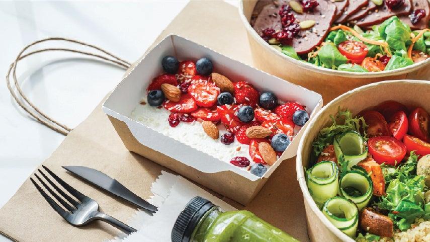 Healthy spread of protein on a table, including yogurt with fruit, and healthy salad with grilled chicken.