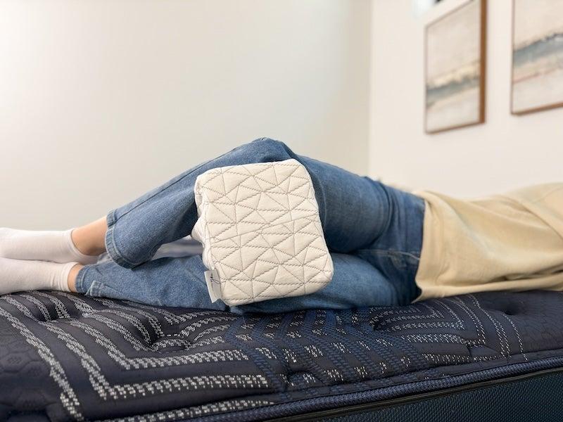 A side sleeper wearing jeans rests with the Coop Sleep Goods knee pillow between their knees