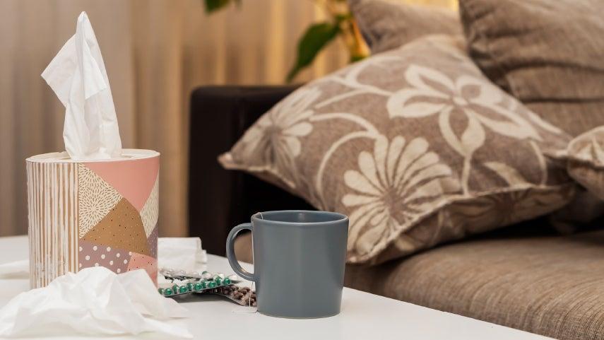 Up close shot of tissues in a holder, along with OTC medicine and a gray coffee mug with hot tea, ready to drink.