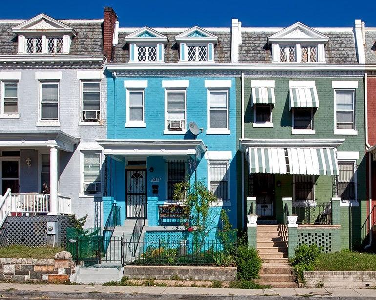 Street view of three colorful row homes in a city neighborhood.