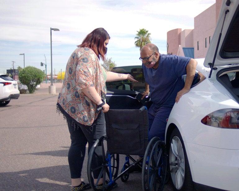 A Lyft driver helps a senior man get out of the car and into a wheel chair at a COVID-19 vaccine event in Arizona.