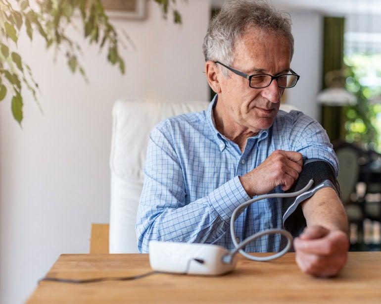 A senior man is sitting down at the kitchen table using a medical device to measure his blood pressure.