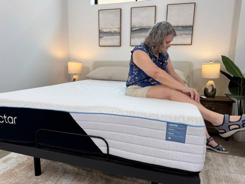 A woman’s feet dangle off the side of a mattress as she sits on the bed