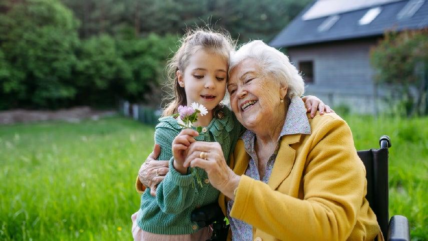 A senior caucasian woman is holding a flower with her granddaughter, enjoying time outside together.