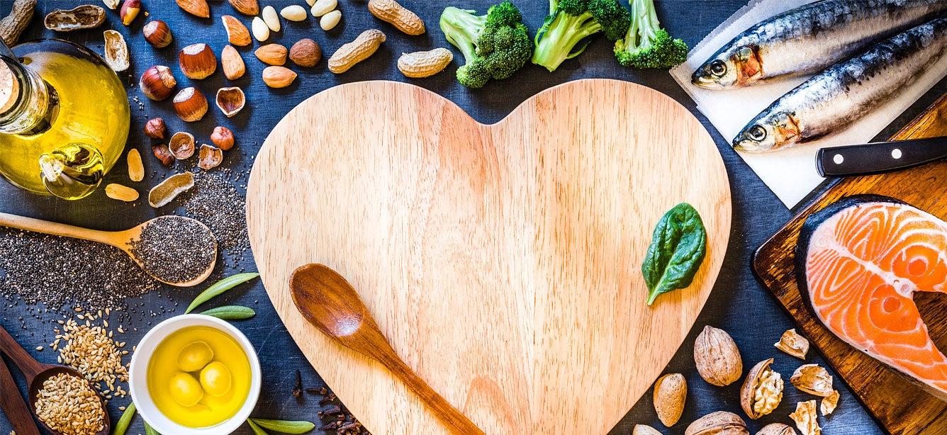 Fresh fruit and healthy food, rest on the outside of a wooden cutting board in the shape of a heart.