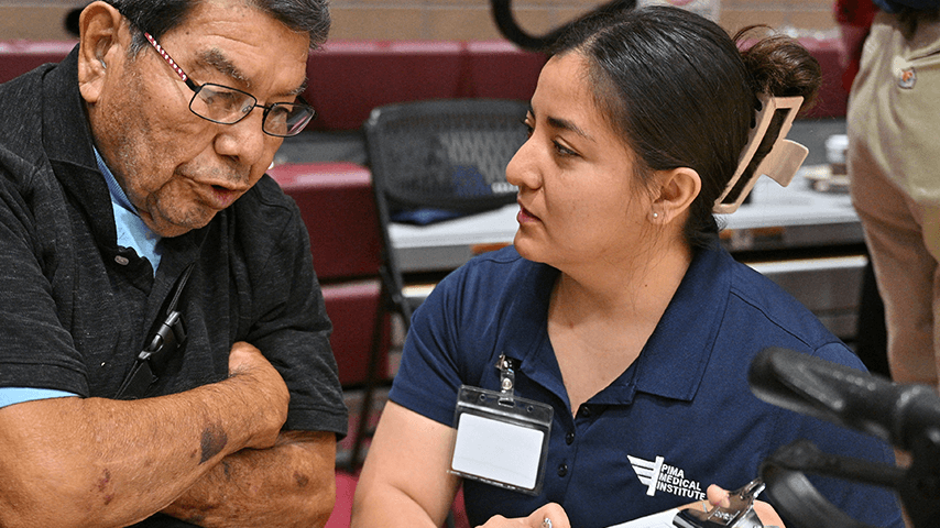 An older man speaks with a woman from the Pima Medical Institute