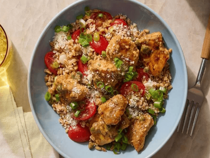 Chicken and rice with veggies in a blue dish beside a glass of water and a fork.