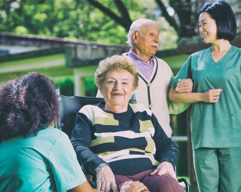 Healthcare workers assist an elderly couple, disabled husband and wife, as they enter the senior center.
