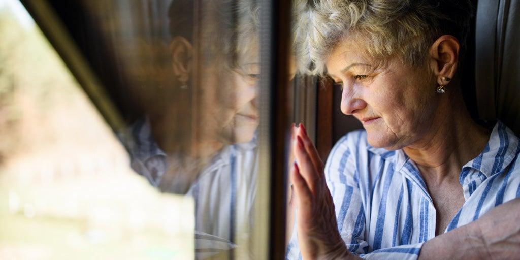 A senior Caucasian woman is at home during the pandemic, staring outside of her window.
