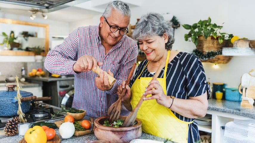Older diverse couple is making a healthy salad in their kitchen for dinner.