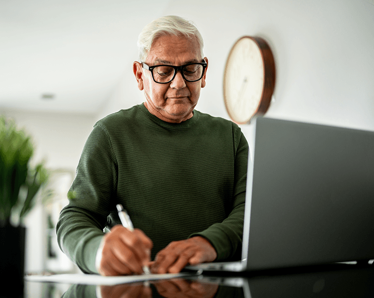 Older man writing in front of a laptop