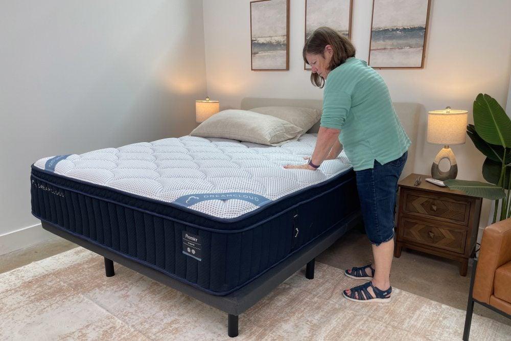 Woman stands next to DreamCloud bed and pushes down on surface of the mattress