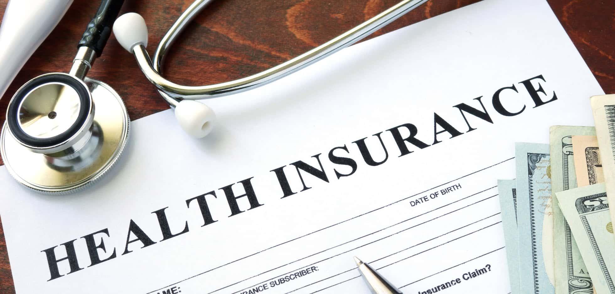 Form with health insurance written at top and stethoscope with dollar bills.