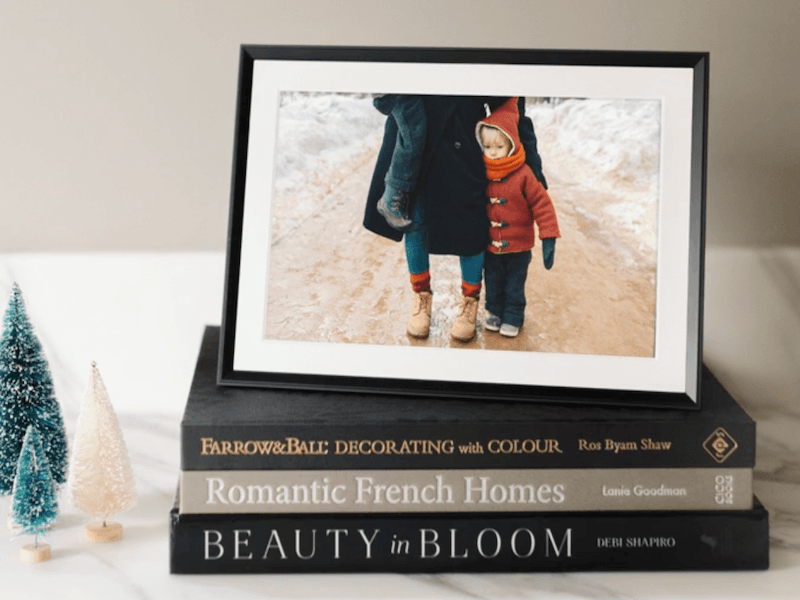 The Aura Carver Mat Digital Picture Frame displayed on top of a stack of books.