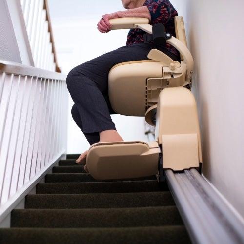 A view from beneath a stair lift as it rises up a staircase carrying a passenger