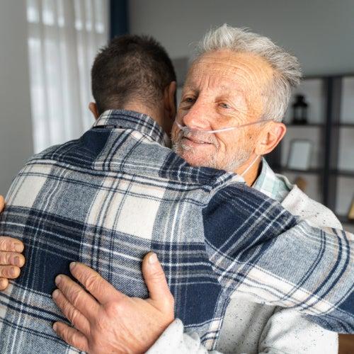 Two men hugging, one is wearing oxygen tubing in his nose