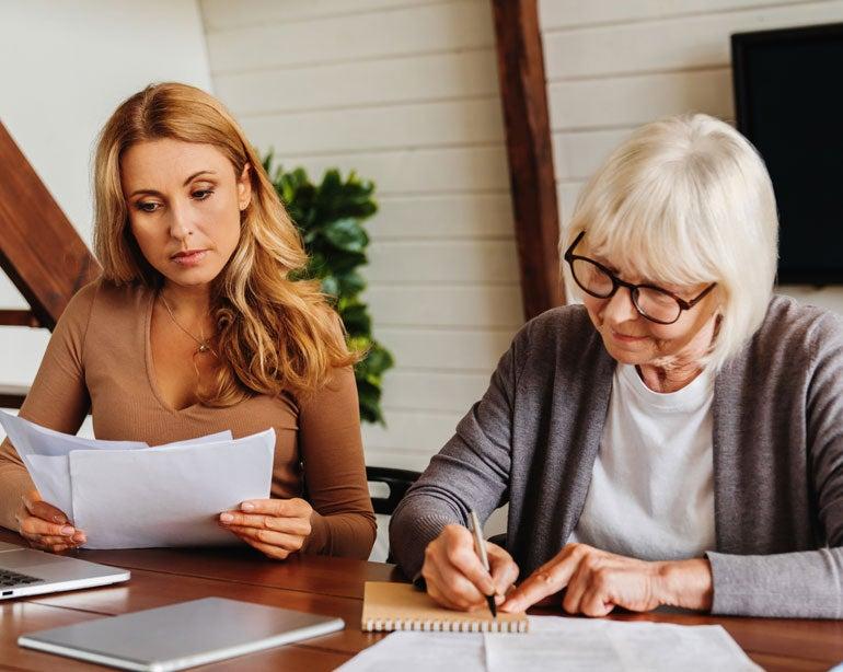 A senior Caucasian woman is receiving help from her caregiver daughter in paying her bills.