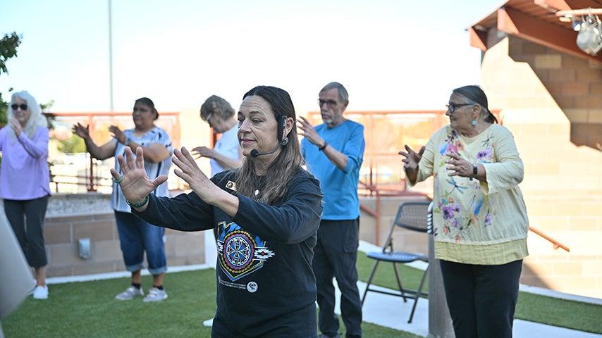 Woman holds out her hands in a tai chi motion. Others in the background of the photo hold their hands in the same position.