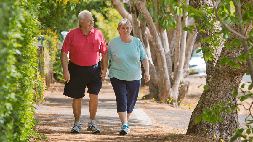 older white man and woman holding hands while walking on tree-lined sidewalk