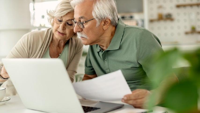 An older adult couple looking at paperwork, making comparisons of income to see if they qualify for dual eligiblity with Medicare/Medicaid.