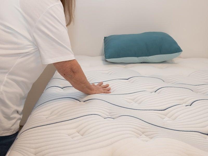A woman presses down on the quilted top of the Bear Elite Hybrid mattress.
