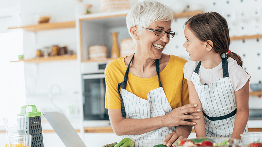 An older woman and younger child laugh while wearing aprons.