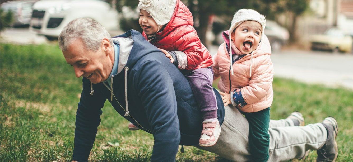 A grandfather holds a plank/pushup position while balancing his two young grandchilden on his back.
