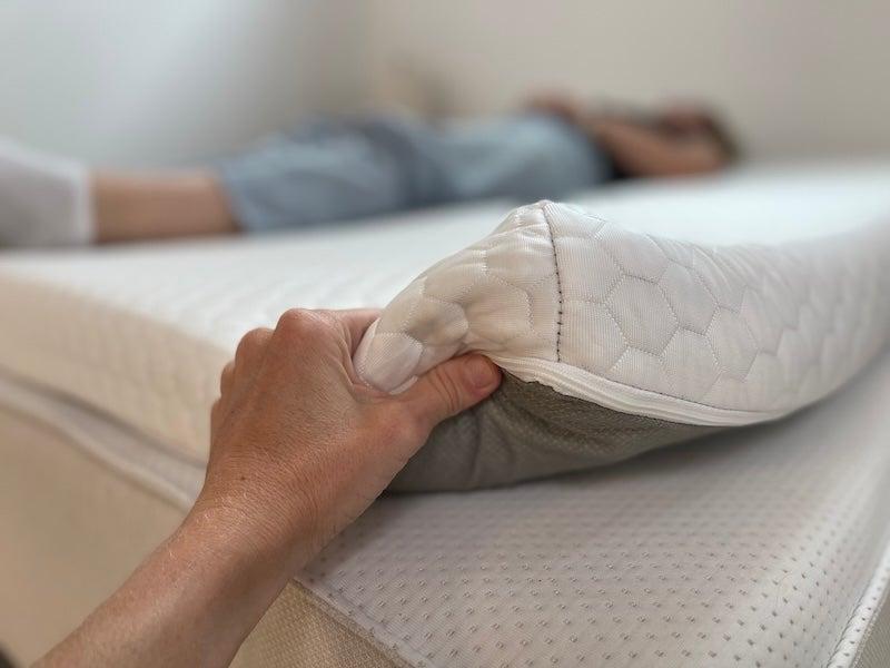A hand lifts up the corner of the Bear Pro mattress topper
