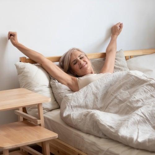 A woman sits up in bed and stretches her arms above her head