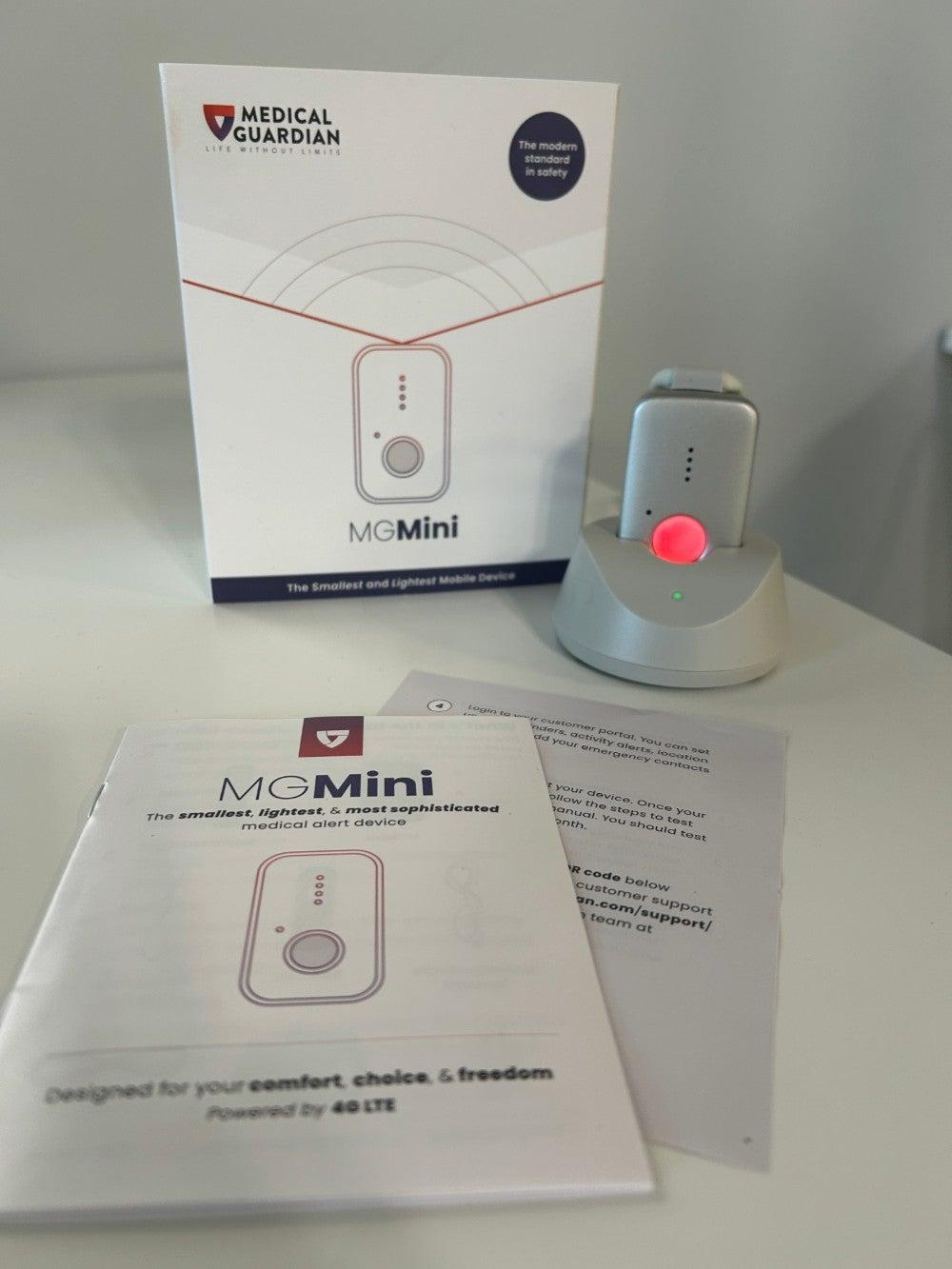 Medical Guardian’s MGMini shines red in its charger, surrounded by its box and user manual
