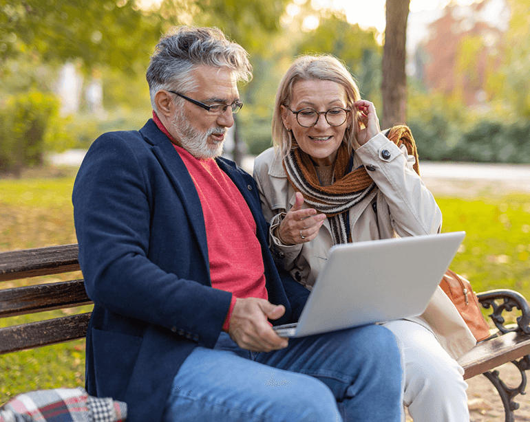 older couple on park bench looking at laptop