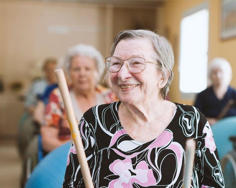 A senior caucasian woman is in a senior center, playing with a drumstick during a group activity.
