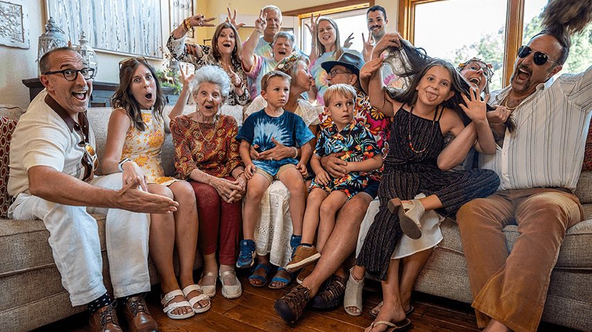 Three generations of a family seated on couch or standing just behind and smiling and cheering