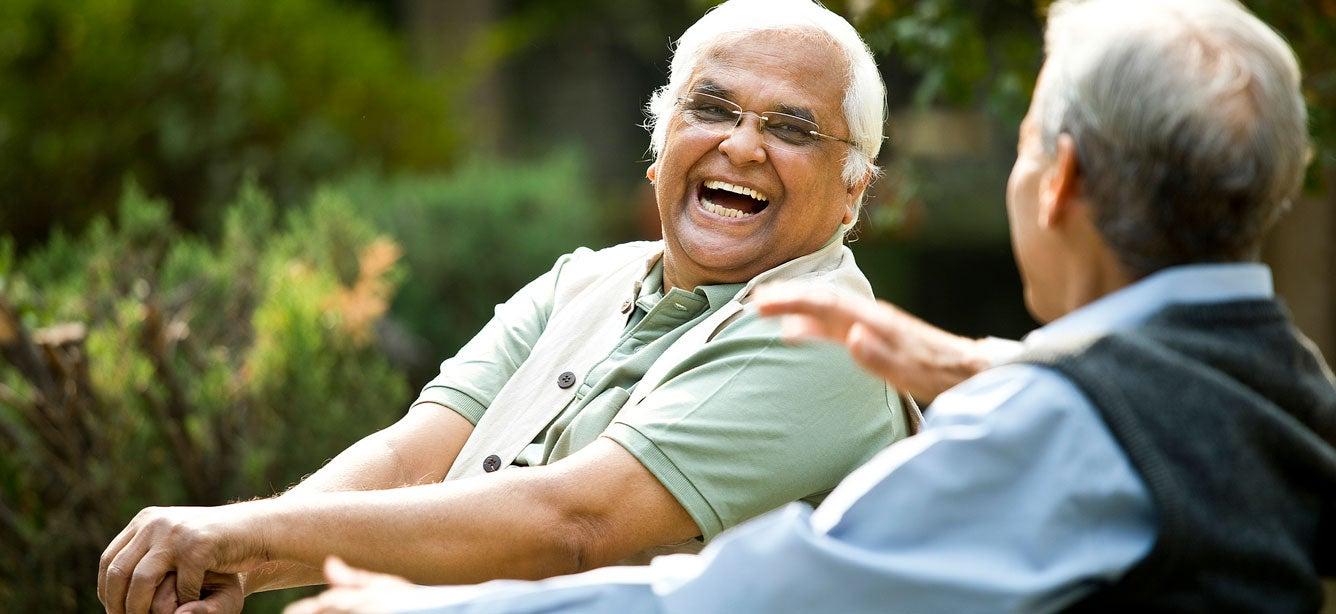Two senior men are sitting on a park bench having a conversation.