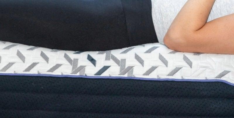 A woman’s torso is shown as she lays at the very edge of the mattress